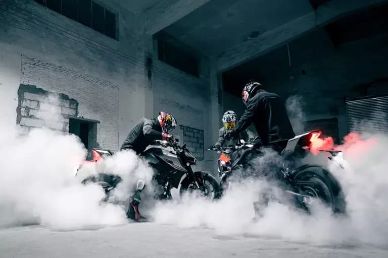 Dos motocicletas KOVE con sus pilotos haciendo quemada de llanta dentro de un edificio abandonado, envueltas en humo blanco