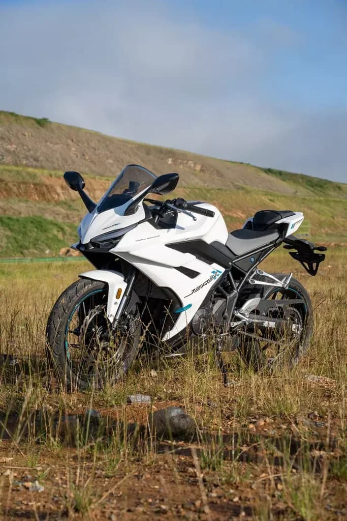 Motocicleta KOVE deportiva blanca con detalles verde agua, estacionada sobre hierba seca