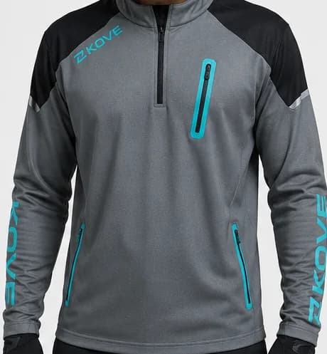 Jersey técnico gris jaspeado de manga larga con cremallera al cuello, paneles negros en los hombros, logotipo KOVE en verde agua en el pecho, bolsillo pectoral y bolsillos de cintura con cremallera verde agua, y la palabra «KOVE» impresa en vertical en cada manga; lo lleva puesto un modelo con guantes negros
